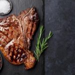Grilled T-bone steak on stone table. Top view with copy space