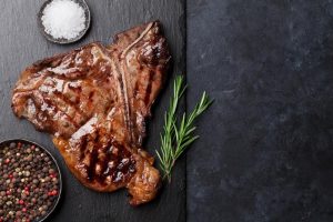Grilled T-bone steak on stone table. Top view with copy space